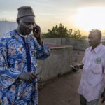 Die Mitarbeiter der "Association Malienne des Expulsés" Amadou Coulibaly (Person links) und Bassekou Siby erhalten einen Anruf vom Direktor des Busbahnhofes, der ihn über das Eintreffen von sechs Rückkehrern informiert, die jetzt auf dem Weg zum AME-Buero sind.